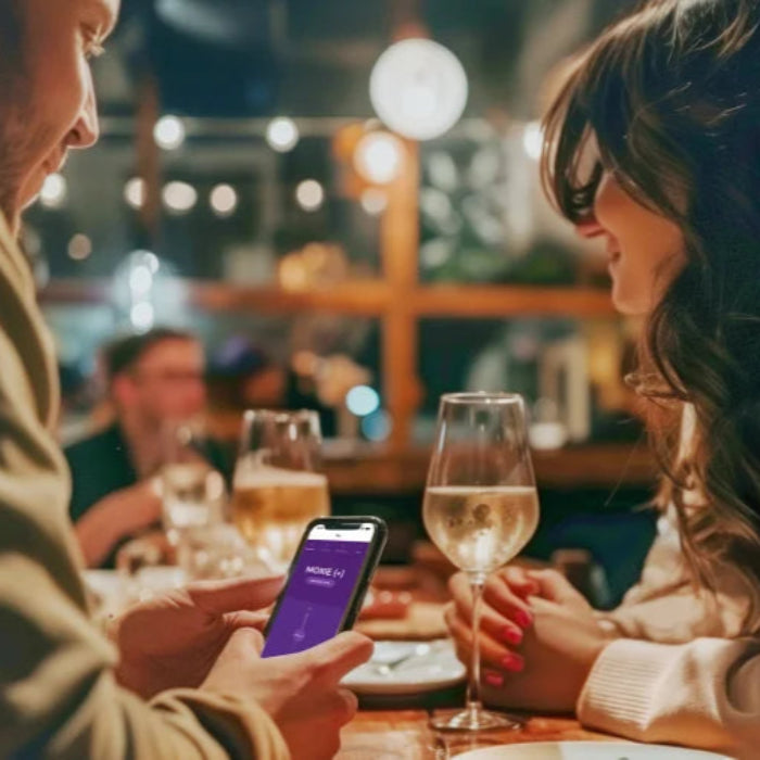 Woman wearing We-Vibe Moxie+ discreetly in panties for hands-free pleasure while out to dinner, partner controlling the vibrator with his phone