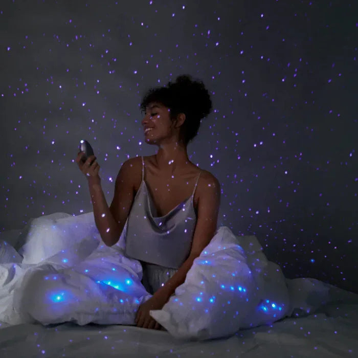 Soft purple starry light from the Pulse Galaxie mood projector casting galaxy-like patterns across a dark bedroom wall, creating a cozy, sensual atmosphere for intimate play. 