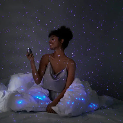Soft purple starry light from the Pulse Galaxie mood projector casting galaxy-like patterns across a dark bedroom wall, creating a cozy, sensual atmosphere for intimate play. 