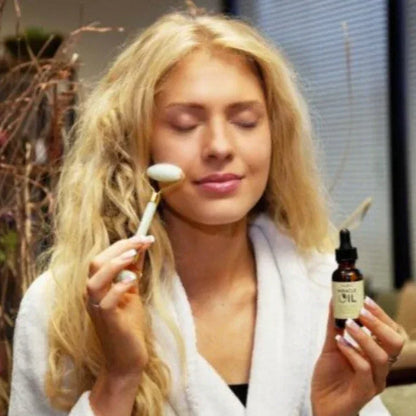 Woman applying a miracle oil with a roller and holding a bottle labeled 'Miracle Oil' in a bathroom spa setting.